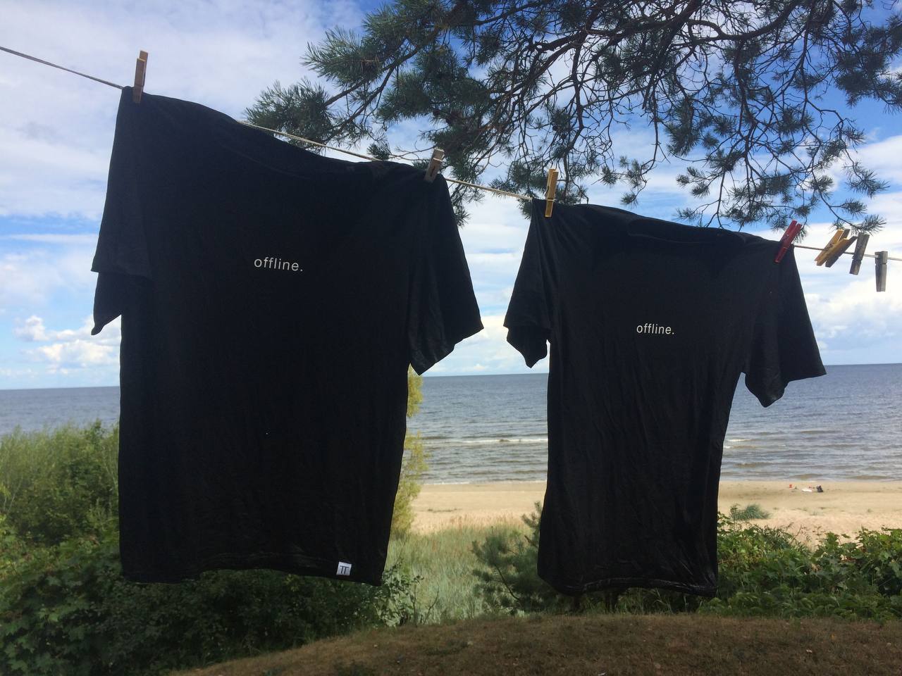 Two t-shirts printed 'offline.' hanging on a clothesline by the lake